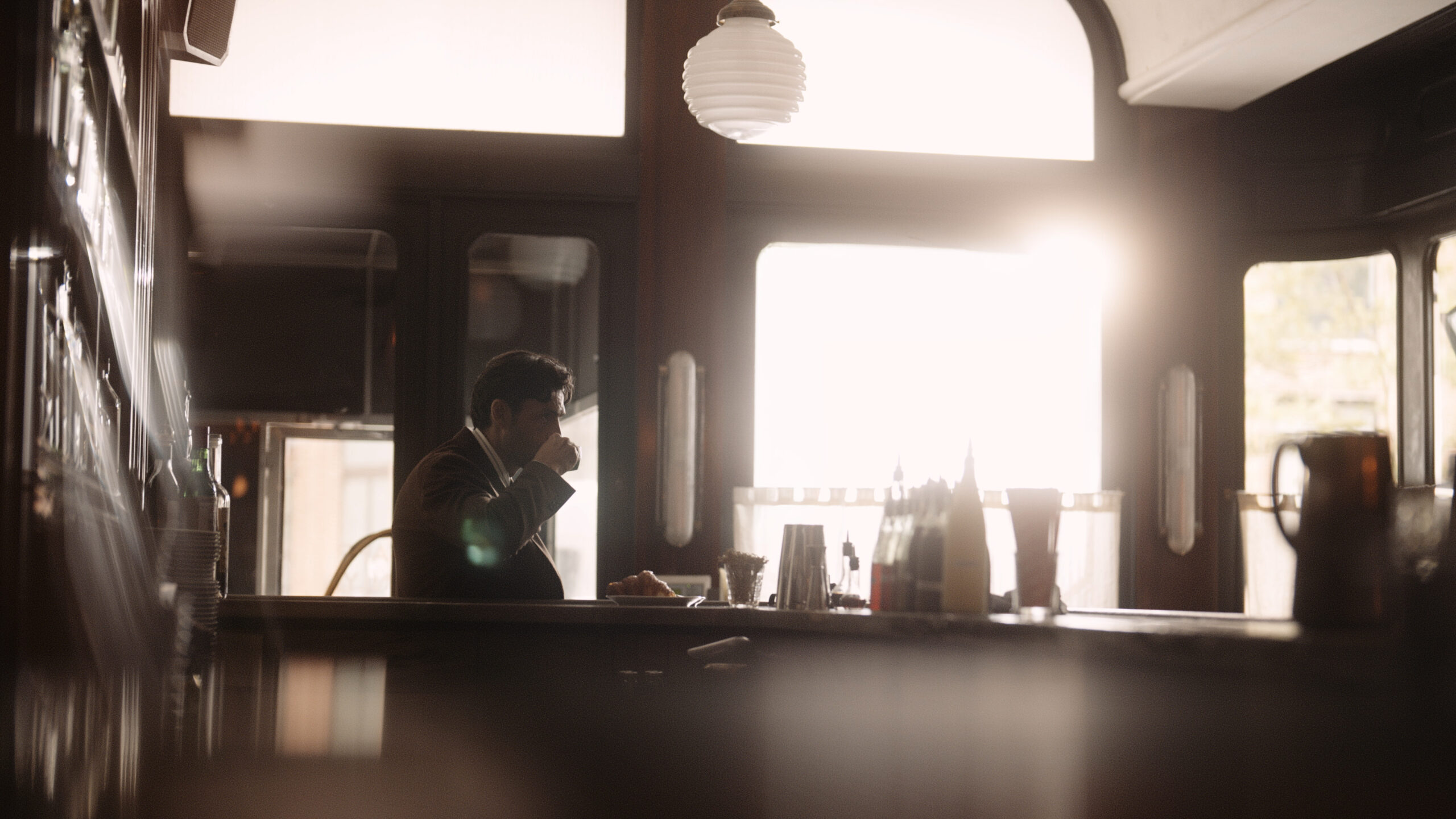 Peter Badenhop in a houndstooth jacket leaning across a table at Frenchette NYC, Madison Moehling blurred in the foreground, for the Todd Snyder American Form Fall campaign.
